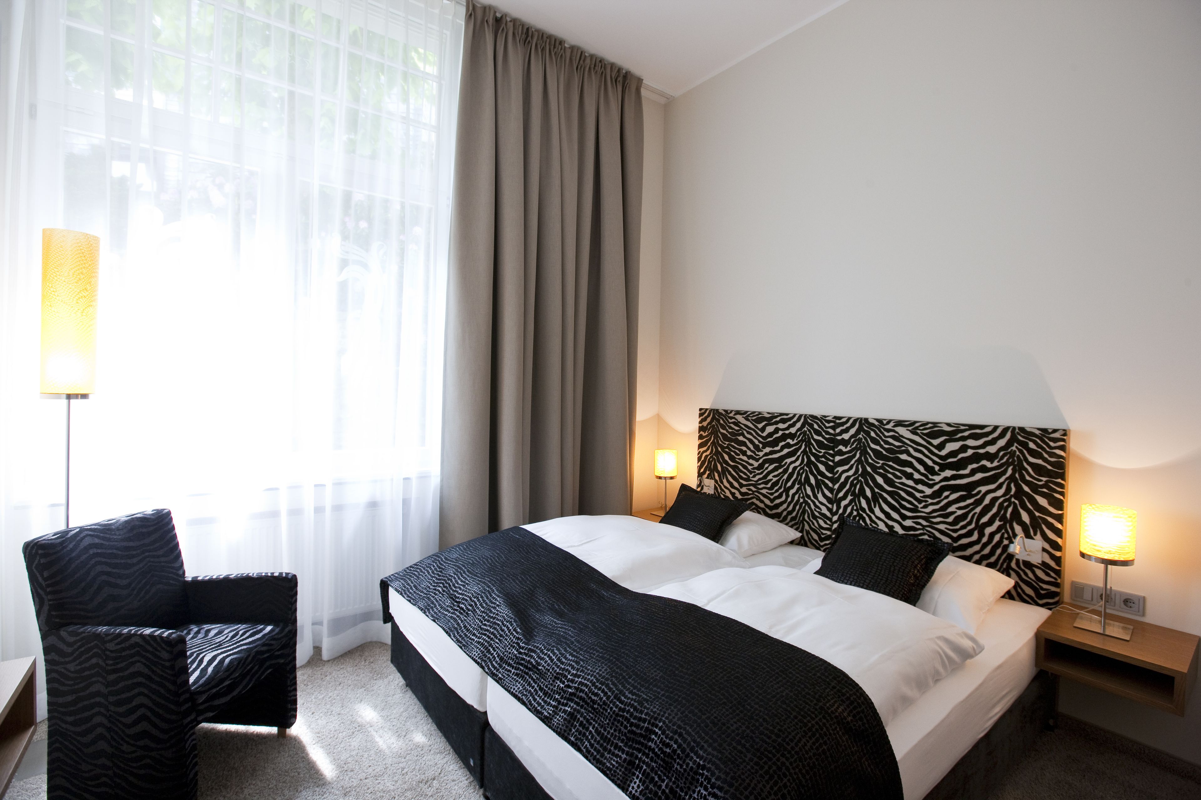A hotel room with a large bed, two bedside tables, a chair, and a zebra-patterned headboard.