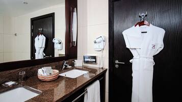 A hotel bathroom with a dark wooden door, a large mirror, a granite countertop, a white sink, a towel rack, and a robe hanging on the wall.