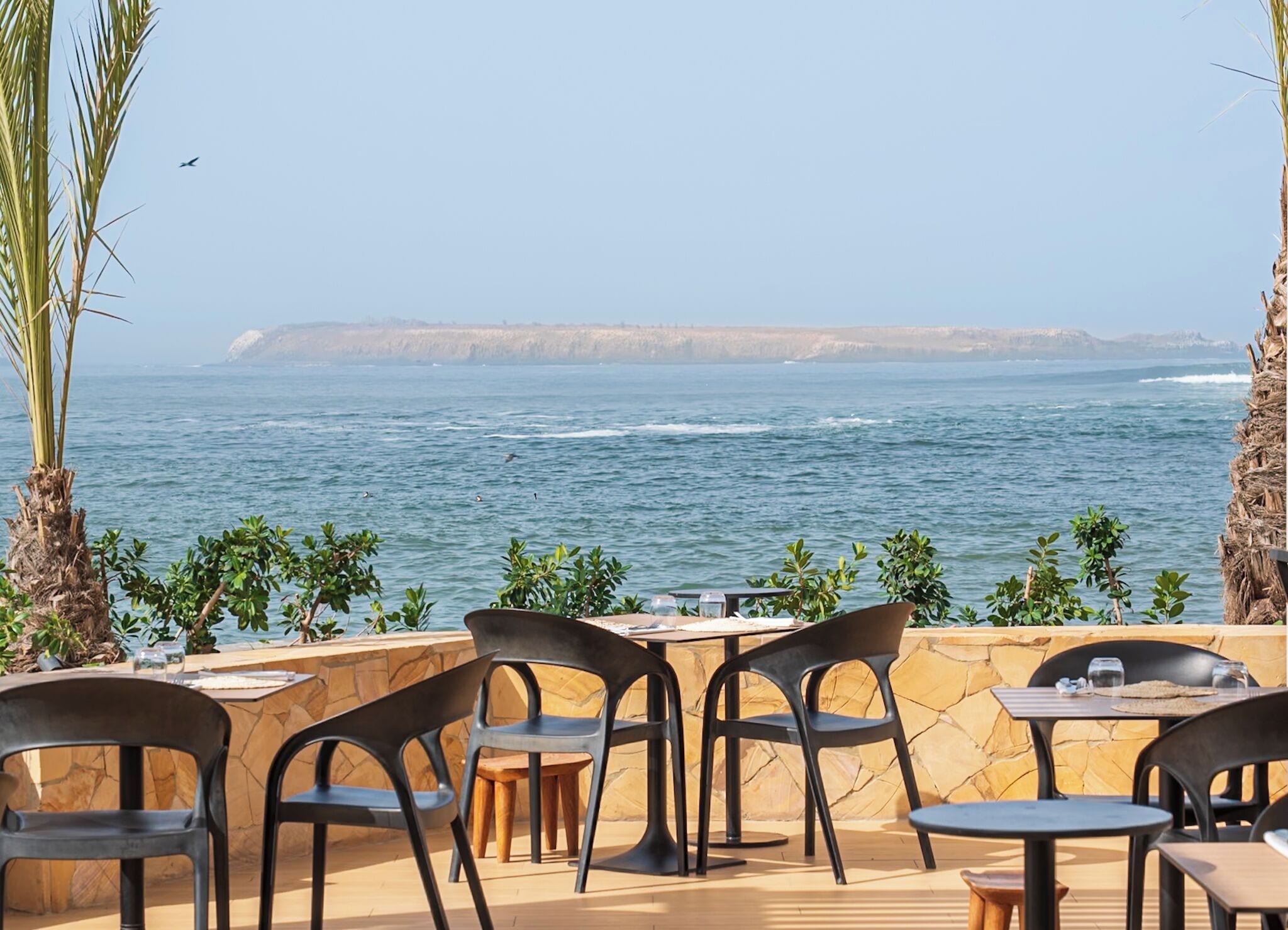 An outdoor seating area with tables and chairs, overlooking a body of water and a distant coastline.