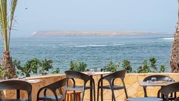 An outdoor seating area with tables and chairs, overlooking a body of water and a distant coastline.