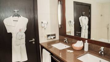 A hotel bathroom with two sinks, a large mirror, a robe hanging on the door, and a towel rack.