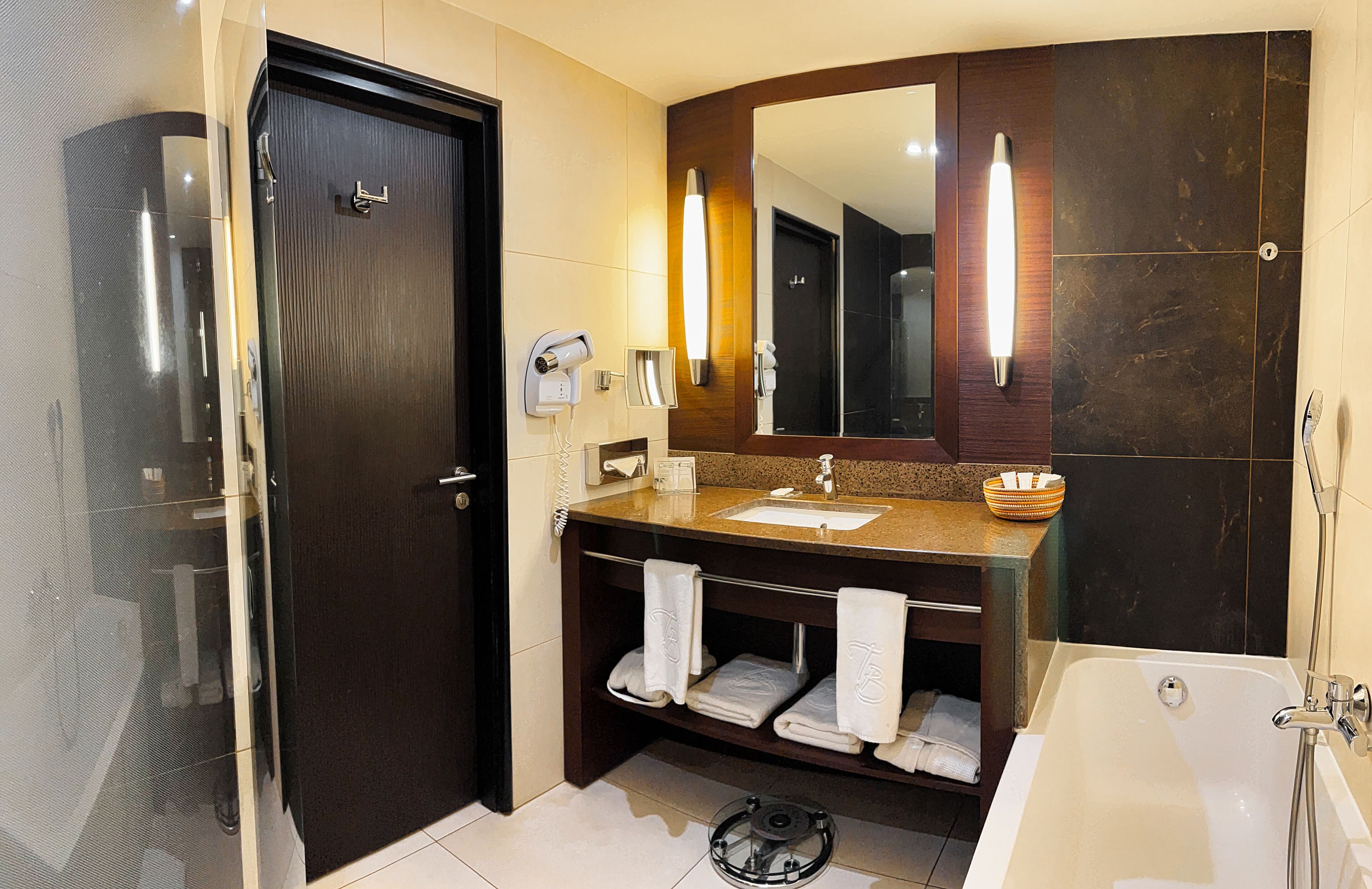 Une salle de bain moderne avec une porte en bois foncé, un grand miroir, un lavabo avec un meuble-vasque et une baignoire.