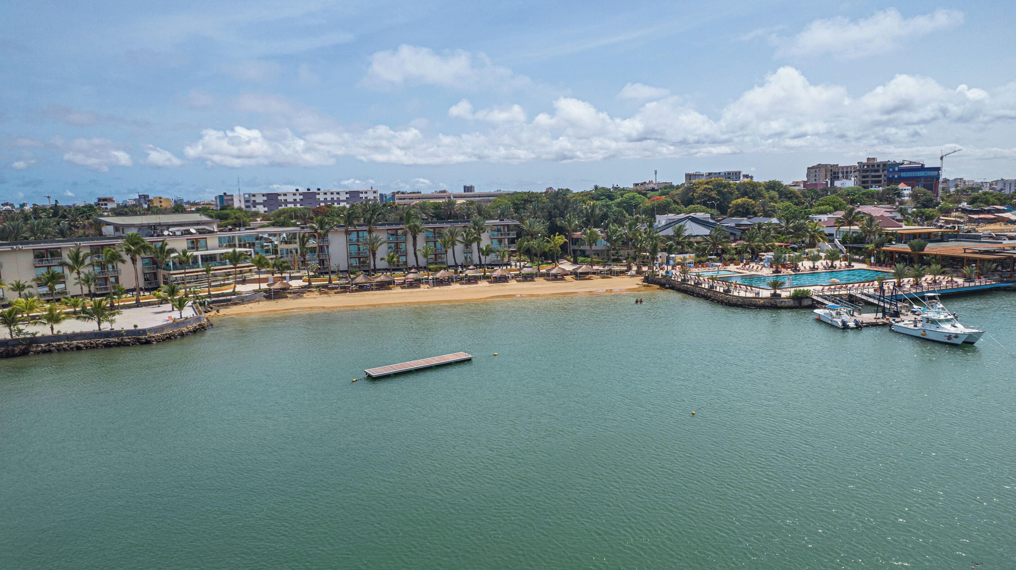 Um resort costeiro com uma praia arenosa, piscina e vários barcos atracados.
