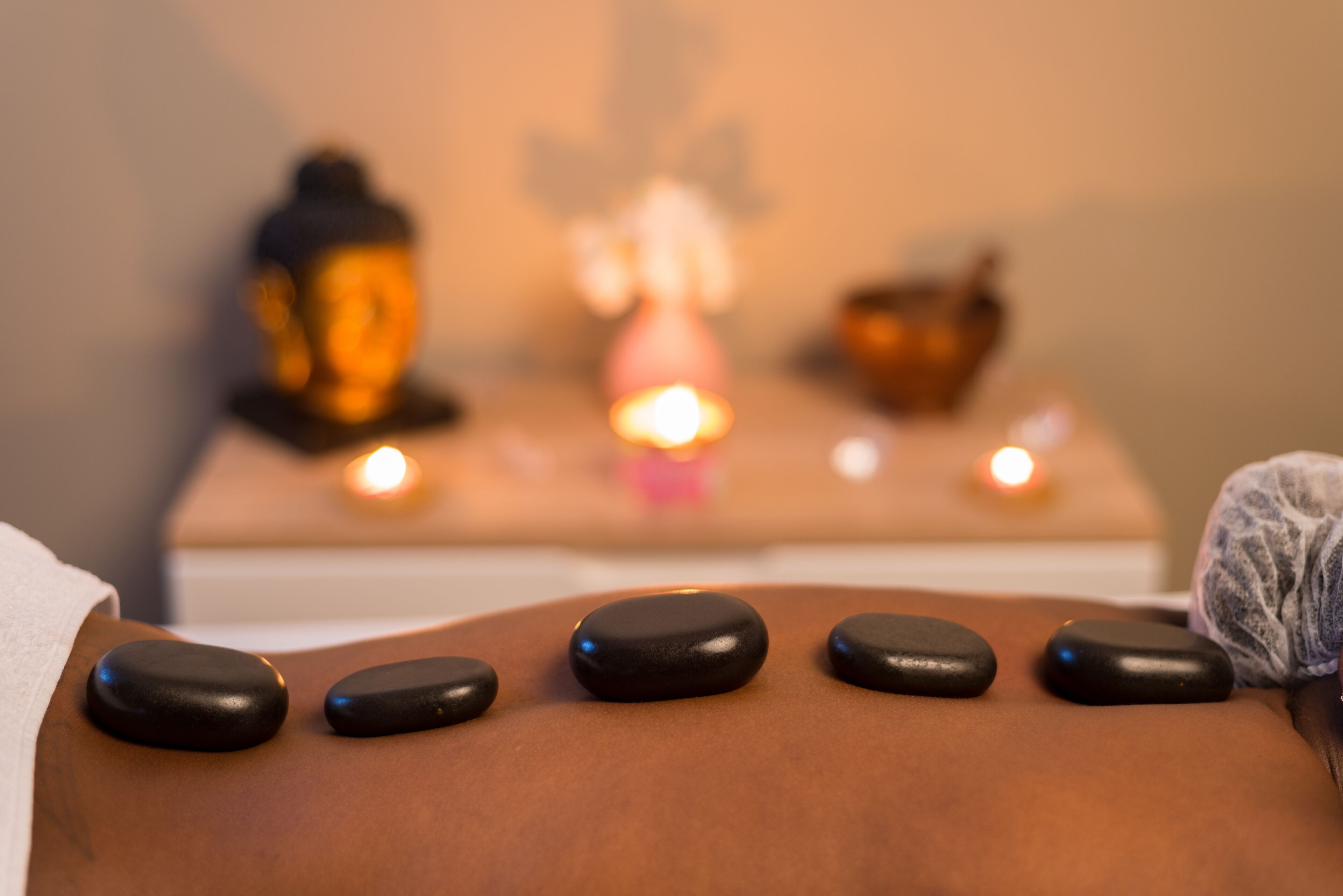 En massagebriks med sorte sten og en Buddha-statue i baggrunden.