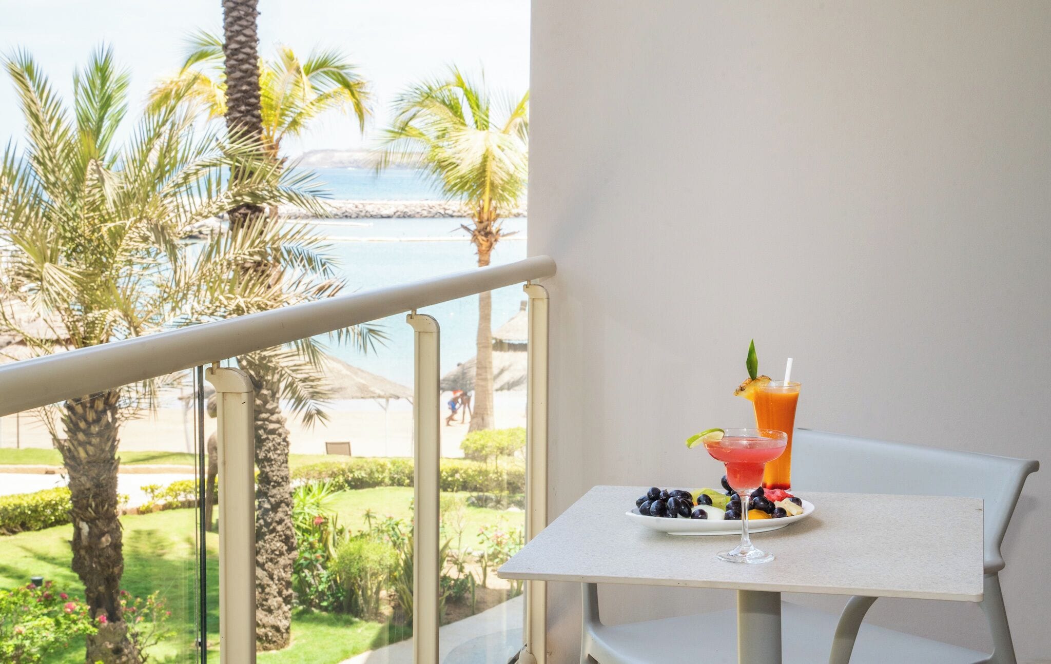 Un balcón con una mesa dispuesta para una comida, una bebida y vistas a palmeras y una masa de agua.