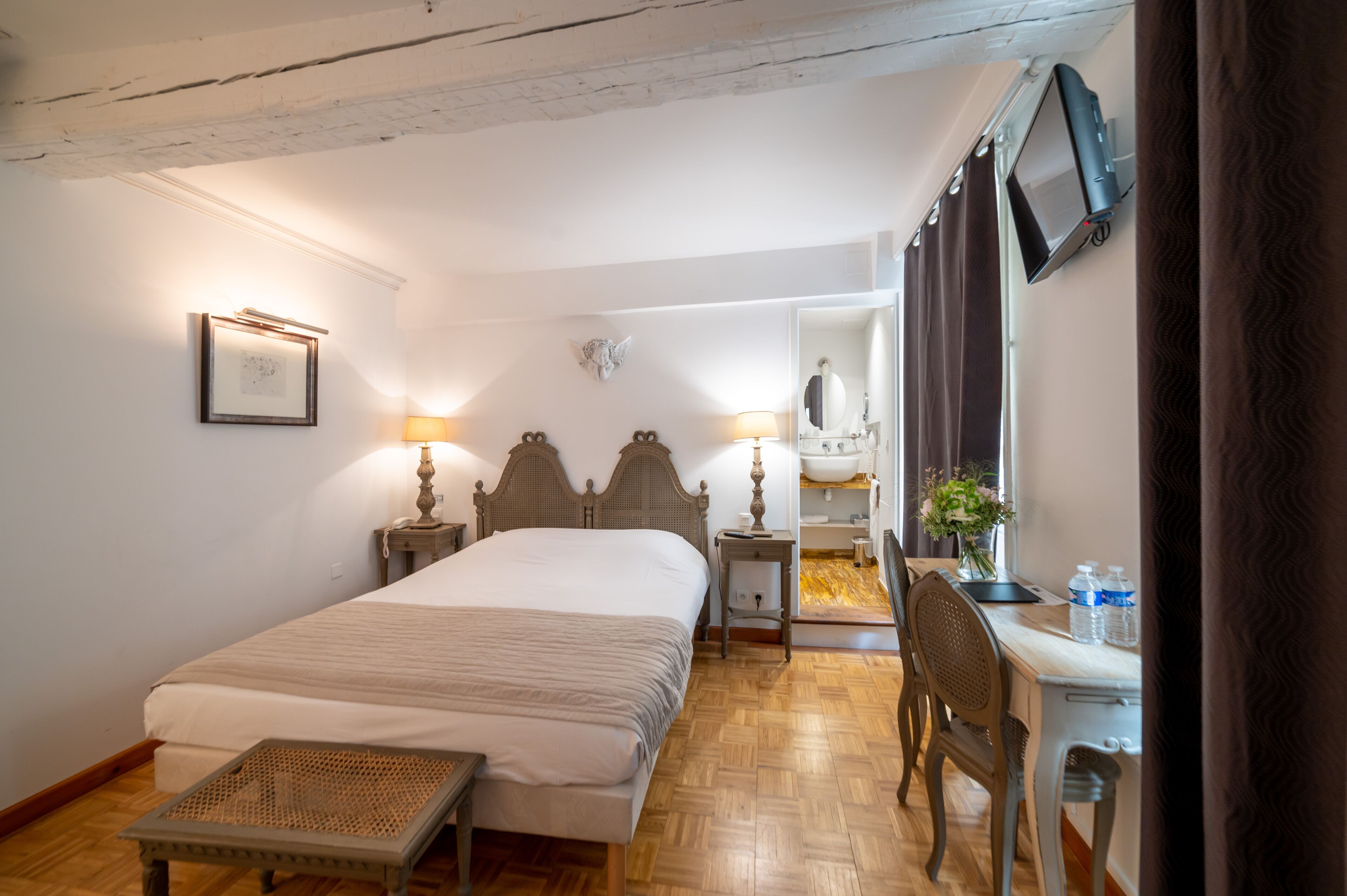 Une chambre avec un grand lit, des lampes de chevet, une tête de lit en bois, un bureau avec une chaise, un miroir et une fenêtre avec des rideaux.
