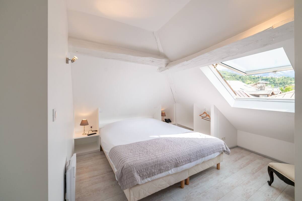 Een slaapkamer met dakraam, een bed, nachtkastjes en een bankje.