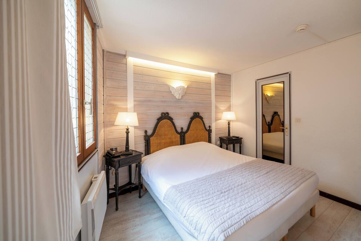 Een verzorgde slaapkamer met een groot bed, twee nachtkastjes met lampen, een wandlamp en een spiegel.