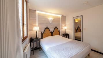 Un dormitorio ordenado con una cama grande, dos mesitas de noche con lámparas, una lámpara de pared y un espejo.