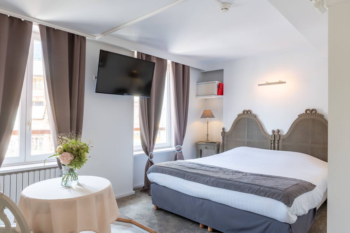 Een hotelkamer met een bed, een aan de muur bevestigde televisie, een nachtkastje met een lamp en een raam met gordijnen.