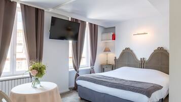 Een hotelkamer met een bed, een aan de muur bevestigde televisie, een nachtkastje met een lamp en een raam met gordijnen.