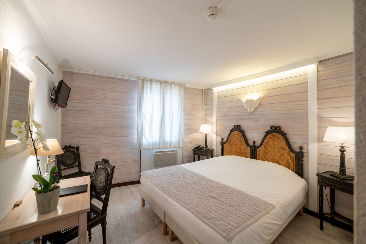 Een hotelkamer met een groot bed, nachtkastjes met lampen, een bureau met stoel, een televisie en een kamerplant.