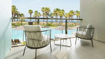Un balcón con dos sillas y una mesa pequeña, con vista a una piscina y palmeras.