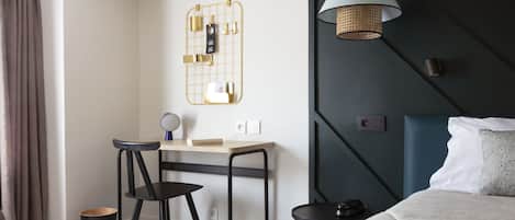Una habitación de hotel moderna con escritorio, dos sillas, cama, mesita de noche, lámpara y una lámpara fijada a la pared.
