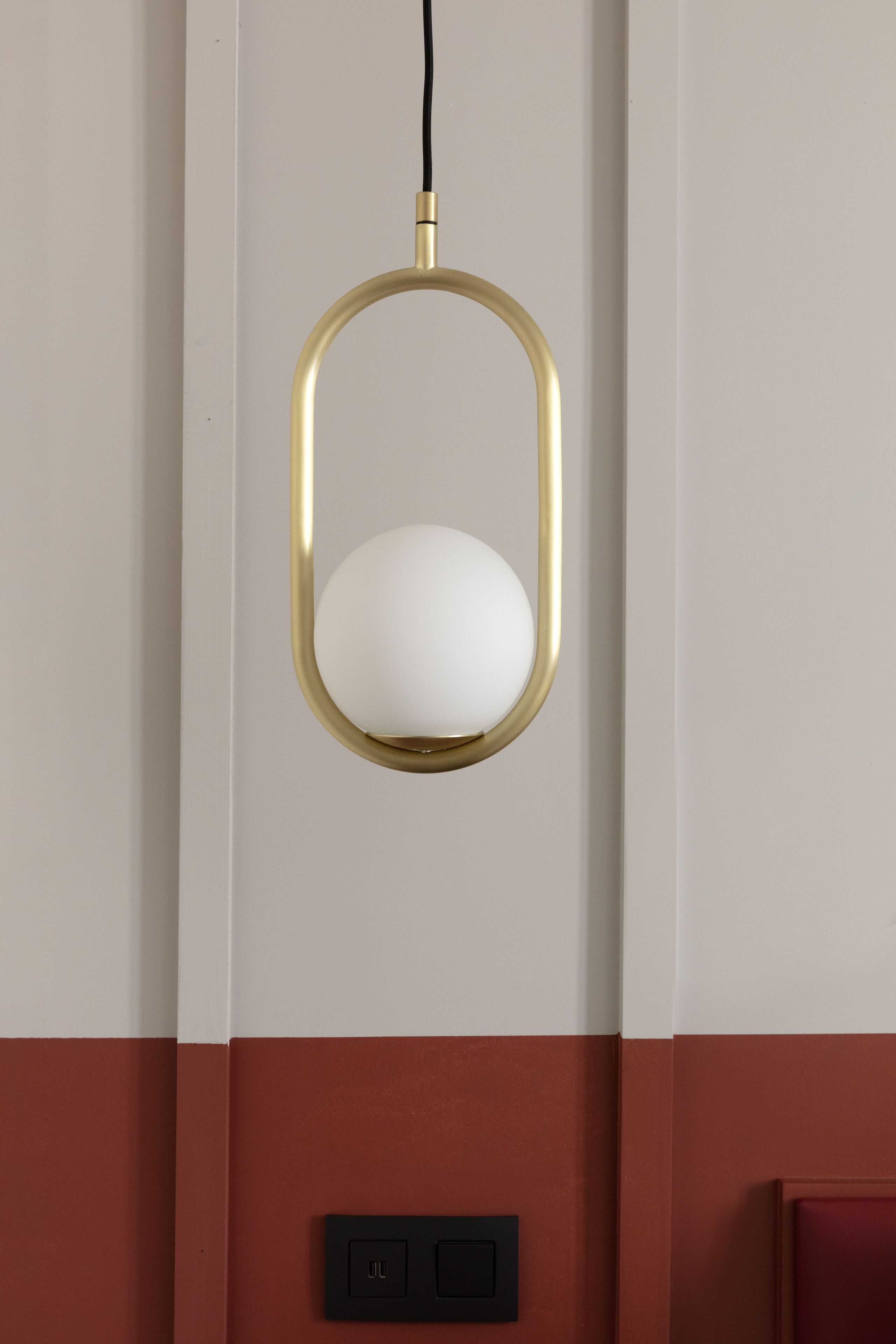 A pendant light with a white shade and a gold frame, mounted on a wall with a red and white panel.