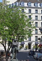 Una estatua de un hombre con vestimenta de época, un árbol y un edificio con múltiples ventanas y balcones.