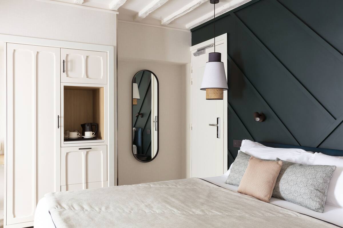 A bedroom with a bed, a wardrobe, a mirror, and a hanging light fixture.