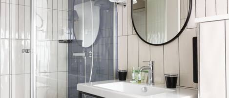A modern bathroom with a glass-enclosed shower, a white sink with a black countertop, and a round mirror on the wall.