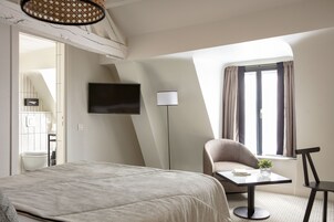 Une chambre d’hôtel avec un lit, un téléviseur fixé au mur, un bureau avec une chaise, une lampe et une fenêtre avec des rideaux.