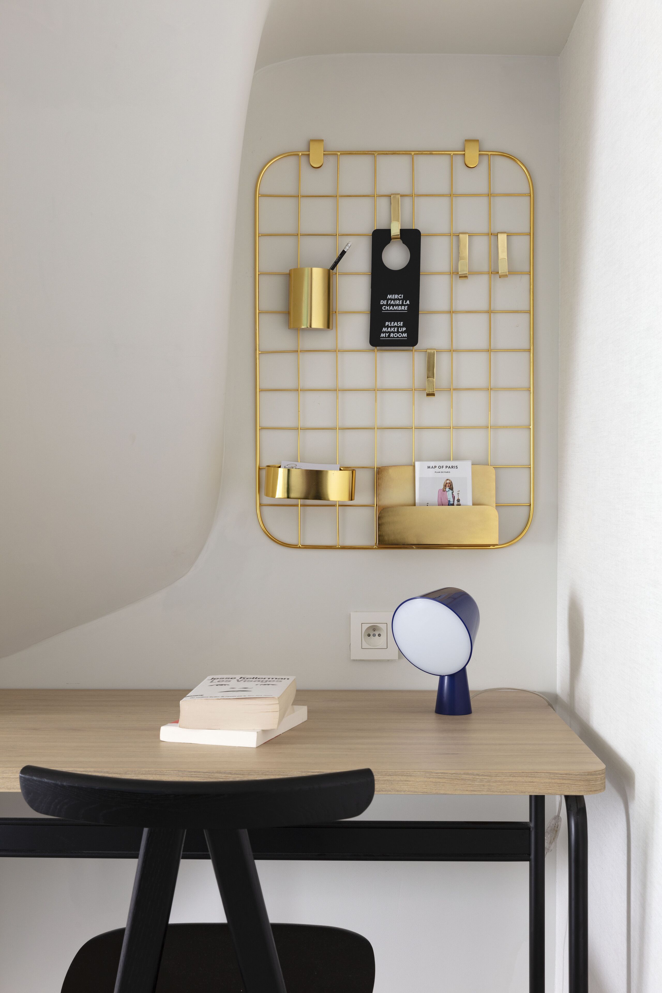 Un bureau avec une étagère en fil de fer doré, une lampe bleue et un livre.