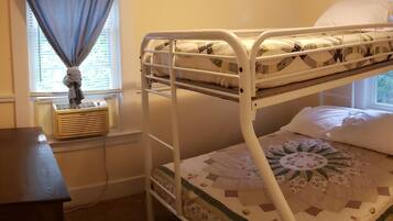 A bunk bed with a patterned quilt, a bedside table, and a window with curtains.