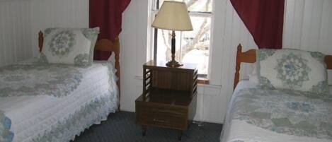 A bedroom with two wooden beds, a nightstand, and a window with red curtains.