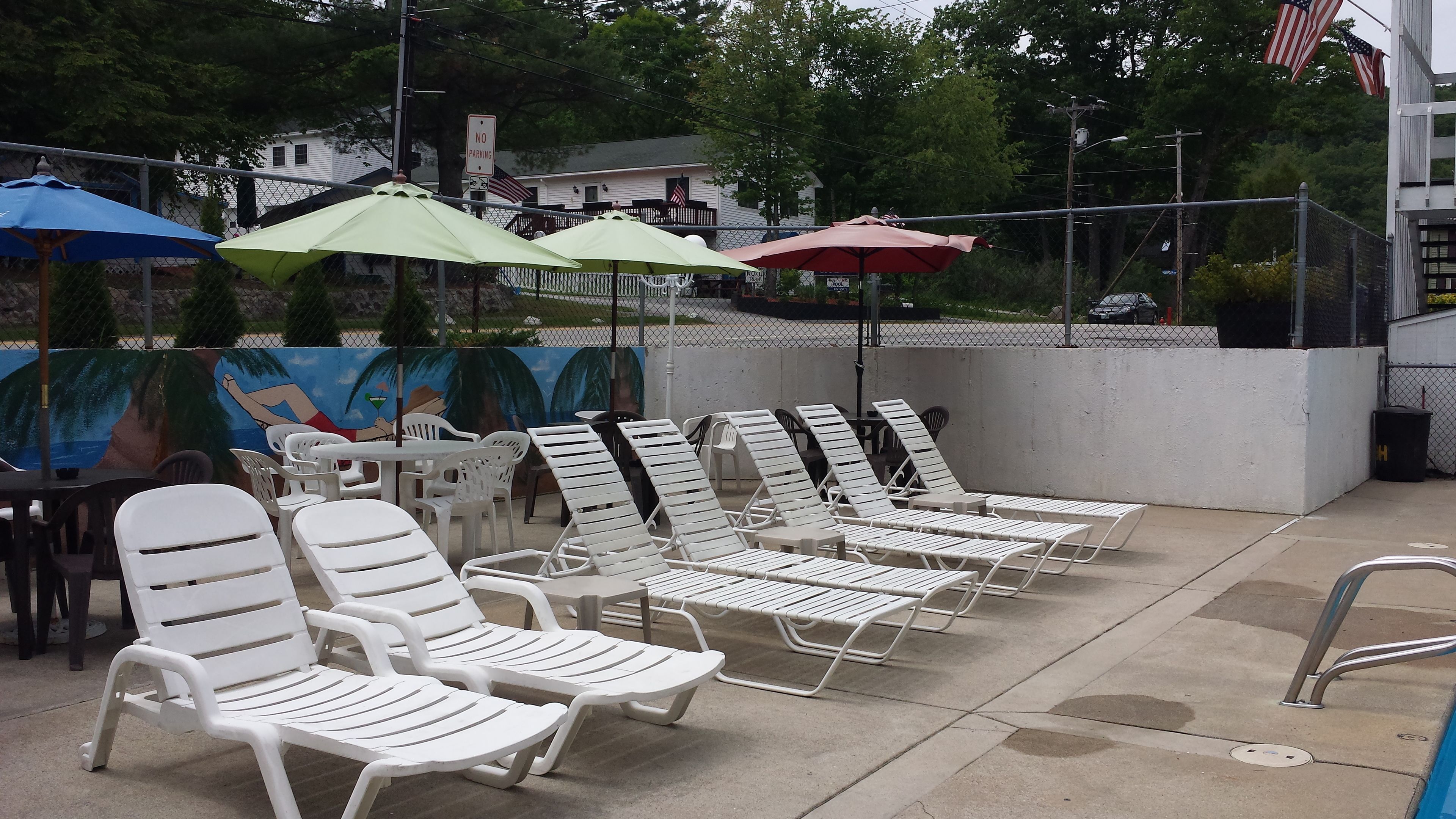 Outdoor lounge chairs and umbrellas, a mural, and a 'No Parking' sign.