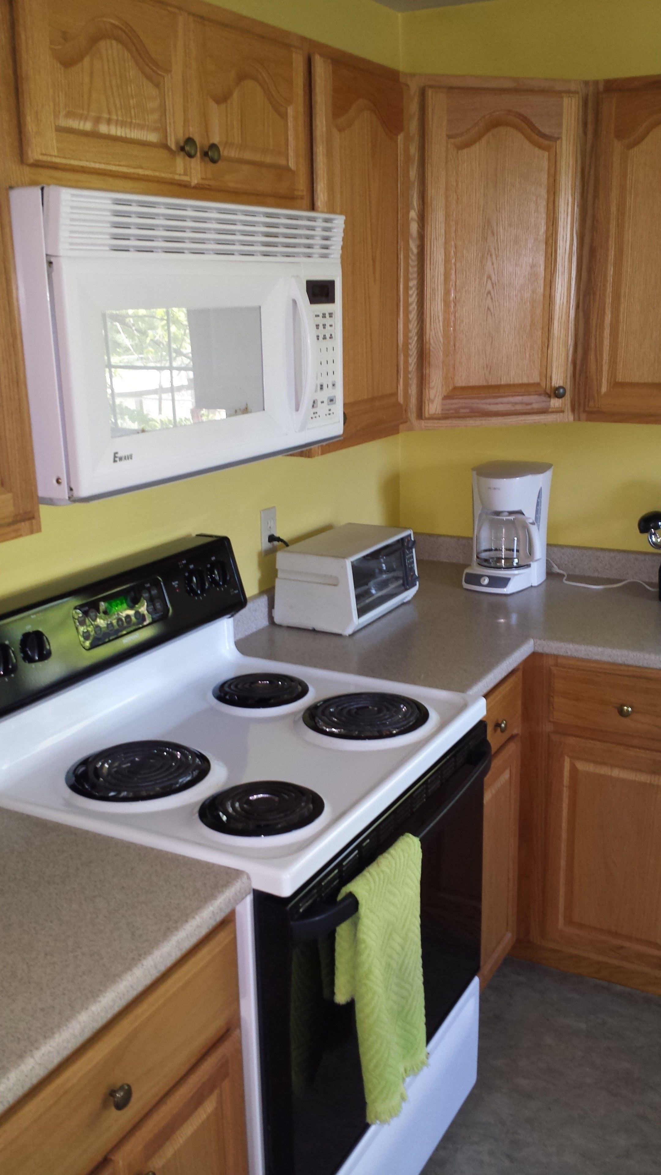 A kitchen with wooden cabinets, a white microwave, a stove with four burners, and a coffee maker.