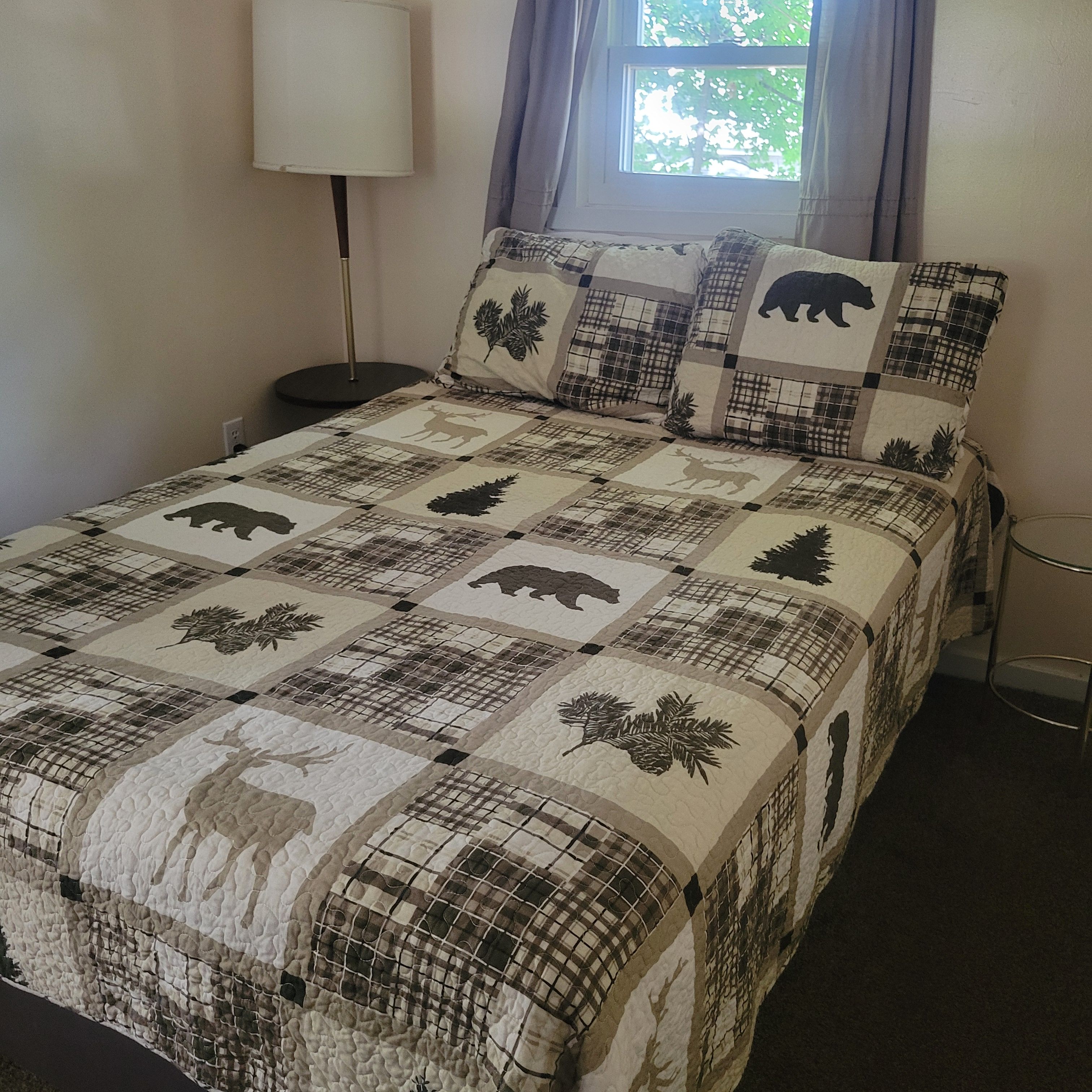 A bed with a quilt featuring animal prints and a lamp beside it.