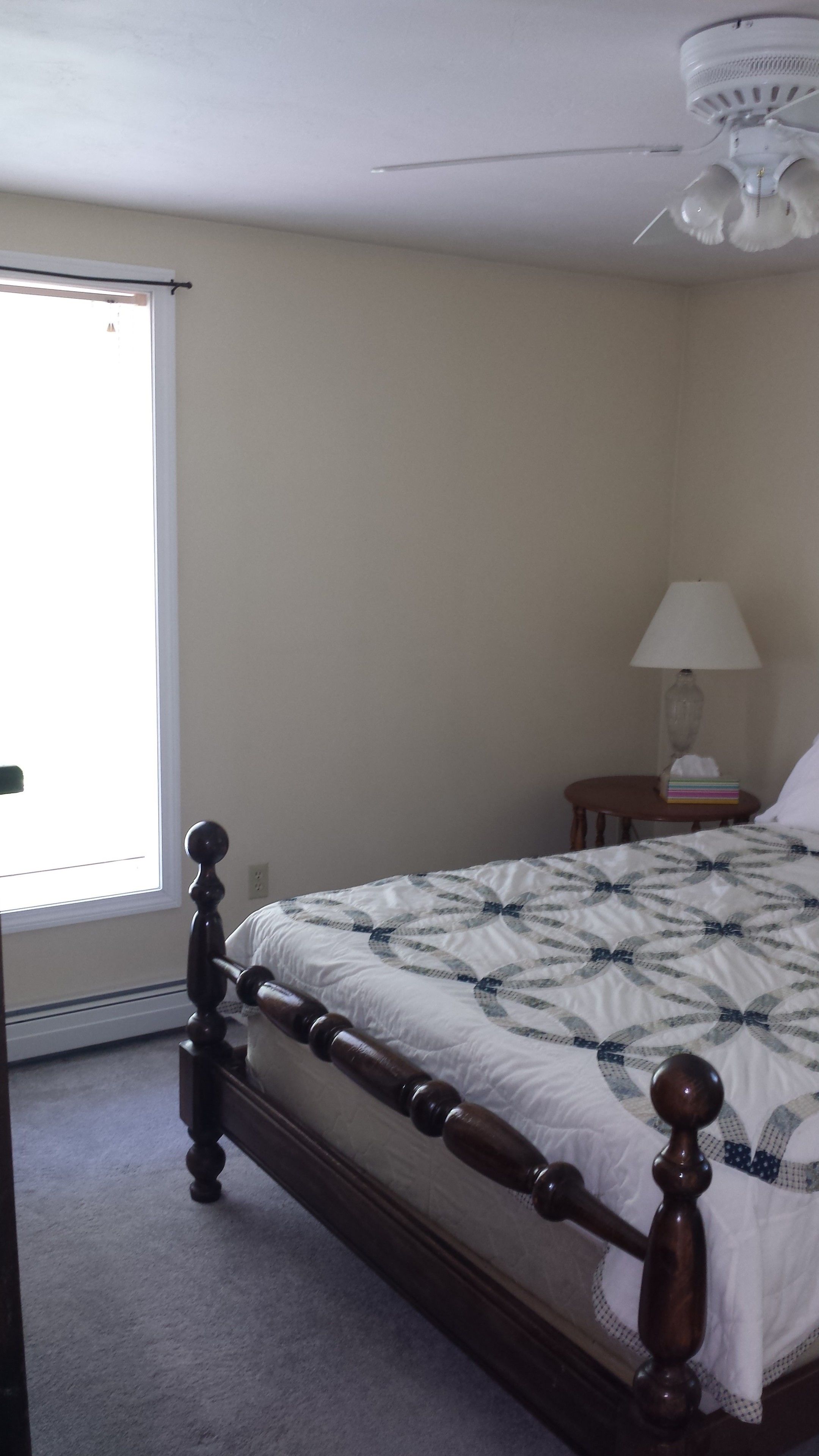 Ein Schlafzimmer mit einem hölzernen Bett, einem Deckenventilator, einem Nachttisch mit Lampe und einem Fenster.