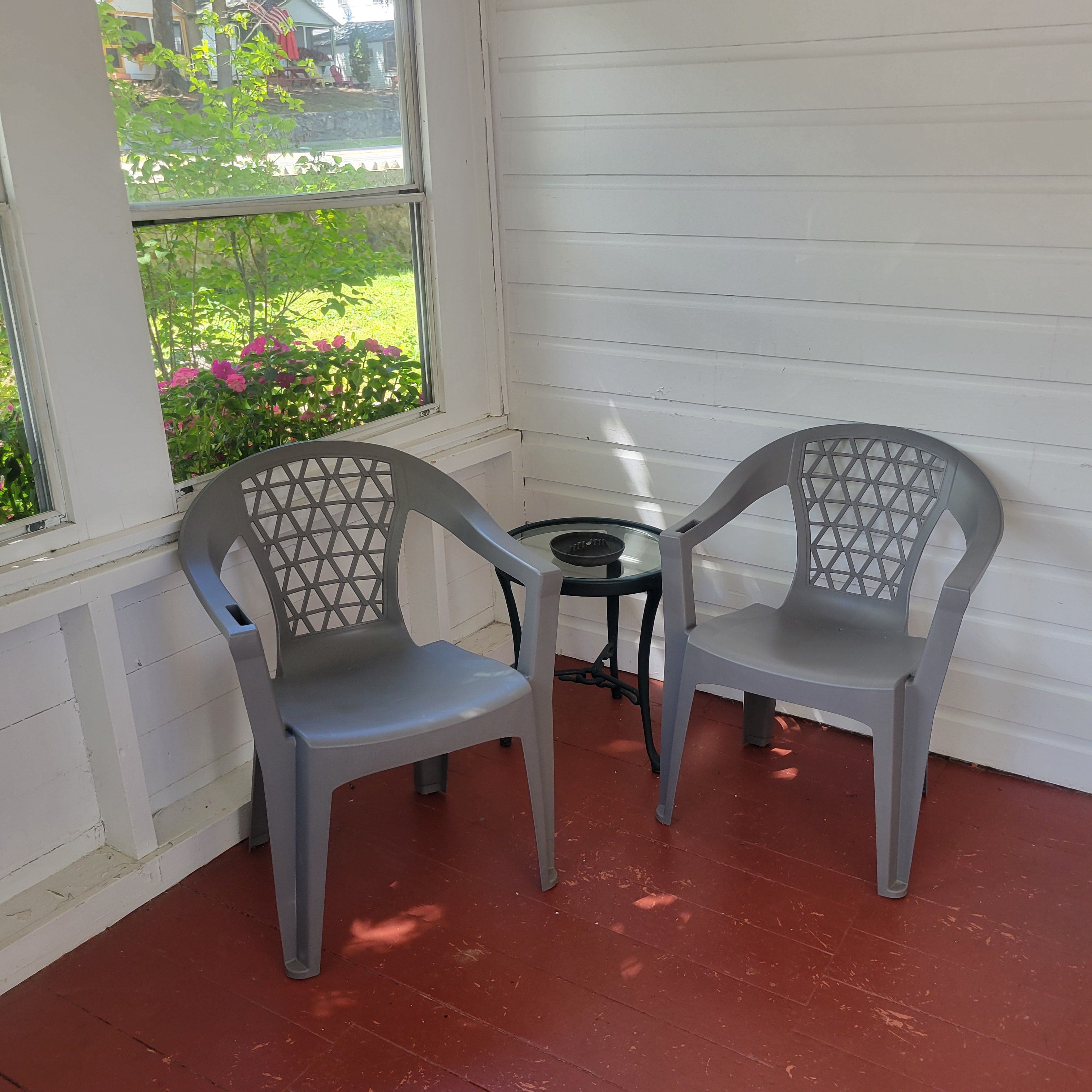 Two gray plastic chairs with a metal table, positioned near a window with a view of a garden.