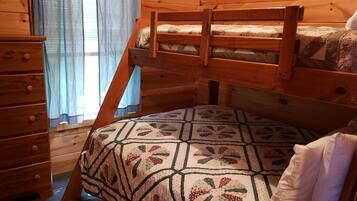 Una cama litera de madera con una colcha estampada con motivos florales y un aparador de madera con cajones.
