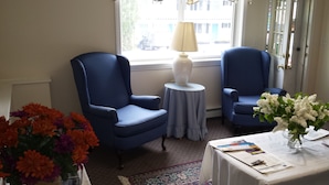 Una habitación con dos sillones azules, una mesita redonda con una lámpara, y un florero con flores blancas.