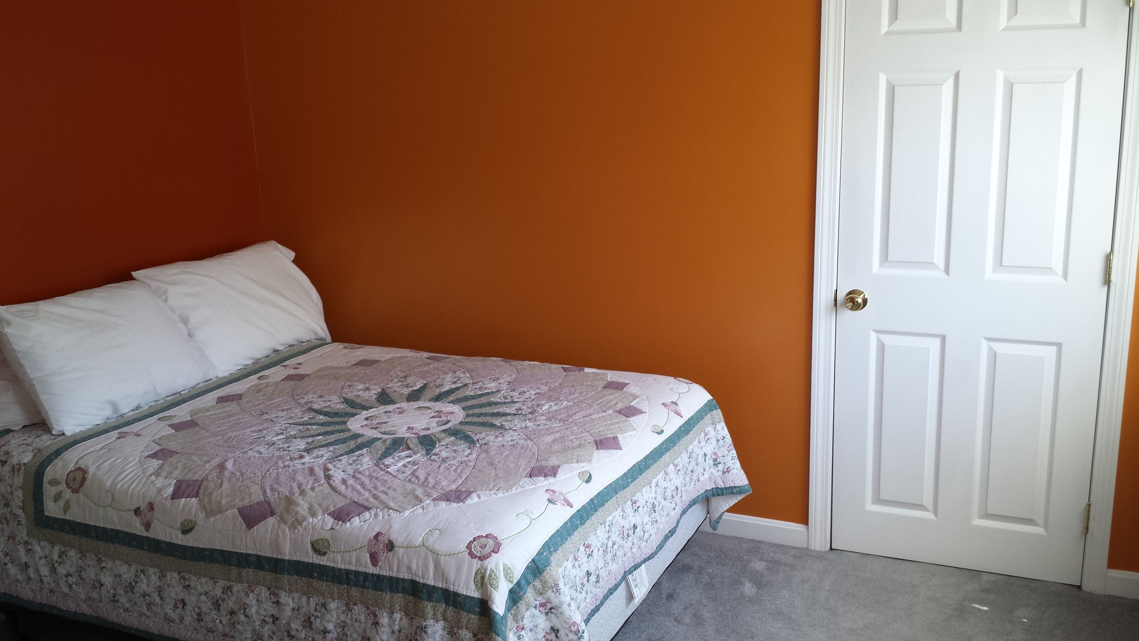 Une chambre à coucher avec un lit, une porte blanche et des murs orange.