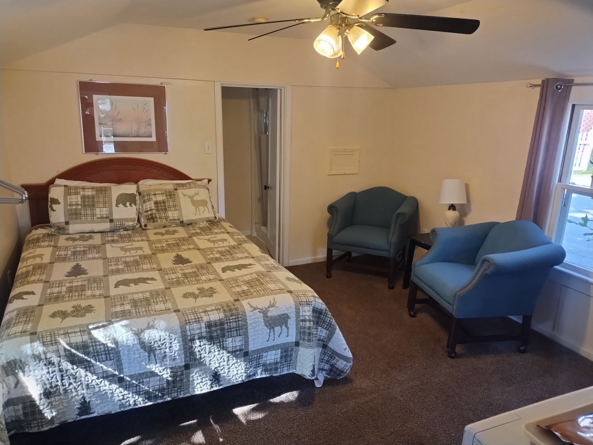 A bedroom with a bed, a chair, a desk, a ceiling fan, and a window.