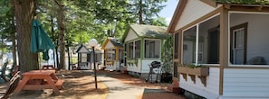 A row of wooden cabins with large windows, a picnic table, and a tree.