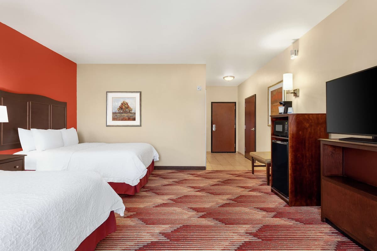 A hotel room with two beds, a TV, a desk, and a microwave.