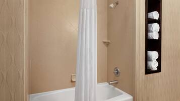 A bathroom with a bathtub, a shower curtain, and a shelf with towels.