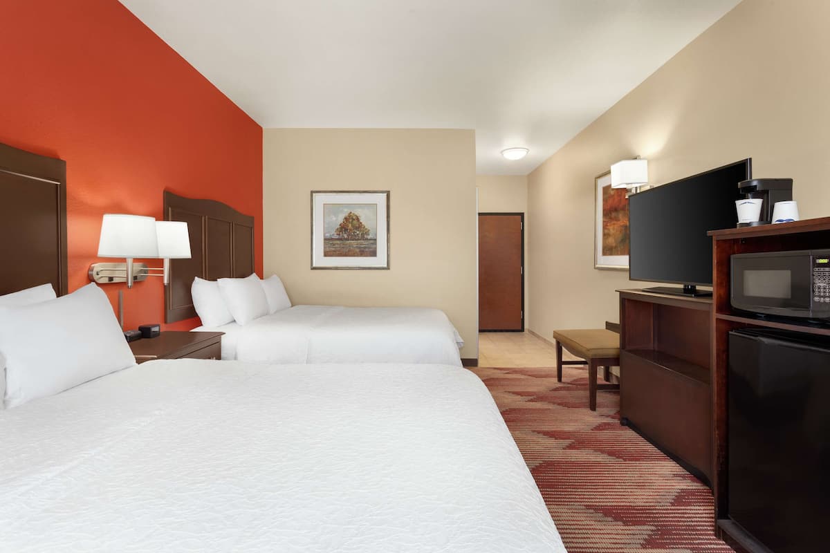 A hotel room with two beds, a television, a microwave, a coffee maker, and a framed picture on the wall.