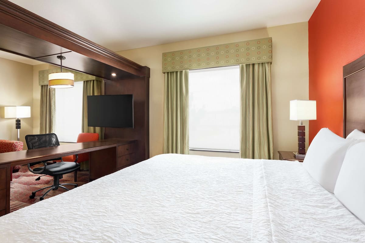 A hotel room with a large bed, a desk with a chair, a television, and a window with curtains.