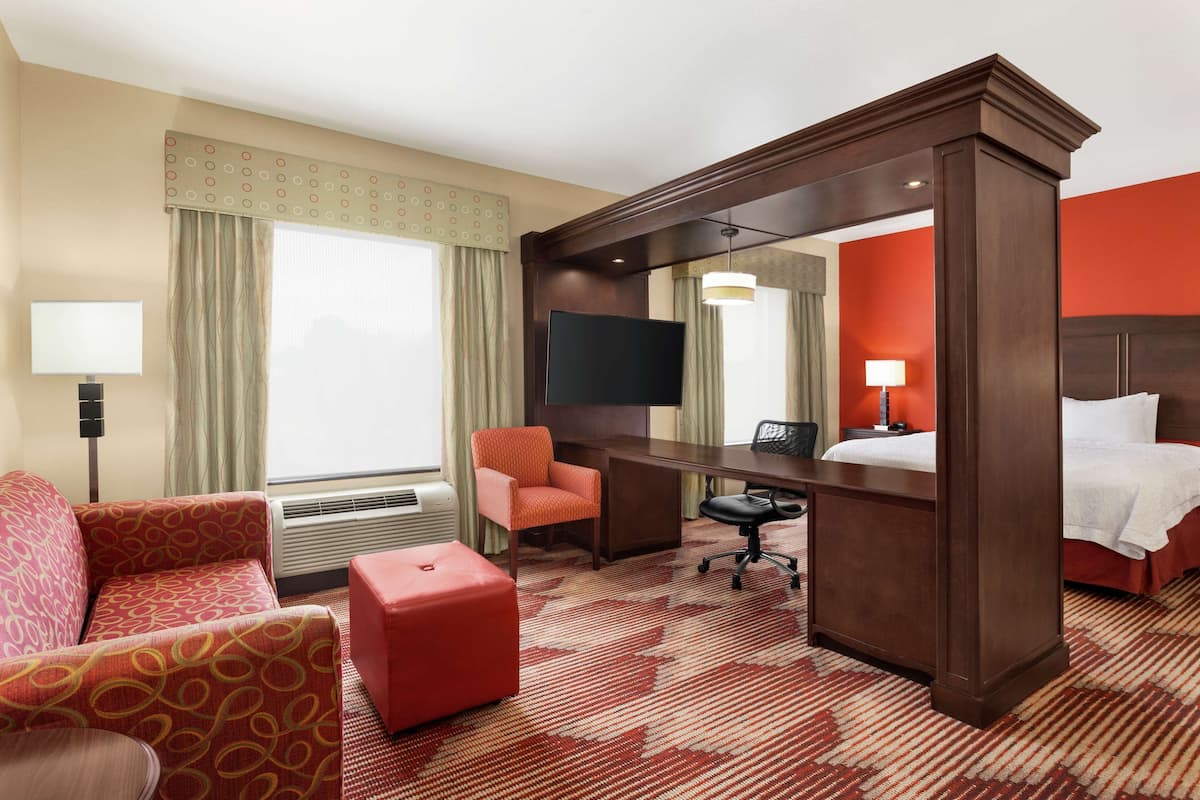 A hotel room with a bed, a desk, a chair, a TV, and a large window with curtains.