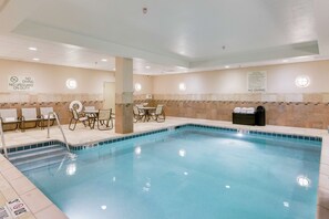 An indoor swimming pool with clear water, surrounded by lounge chairs and a tiled wall with safety signs. - Hilton Garden Inn Milwaukee Airport (Milwaukee)