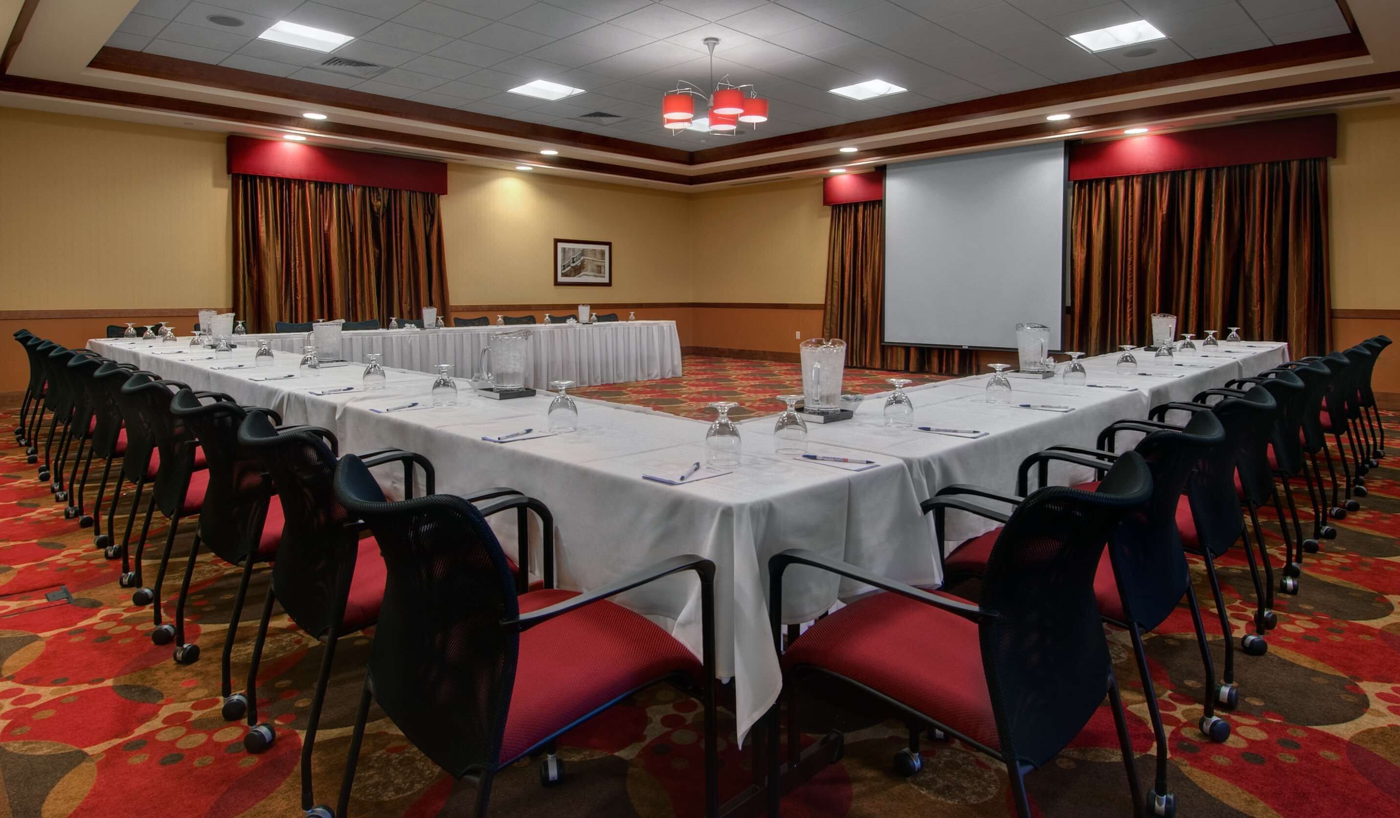 A conference room with a long table, chairs, and a projector screen.