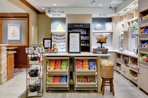 Una tienda de aperitivos con estantes llenos de productos, una zona refrigerada y un cartel de bienvenida.