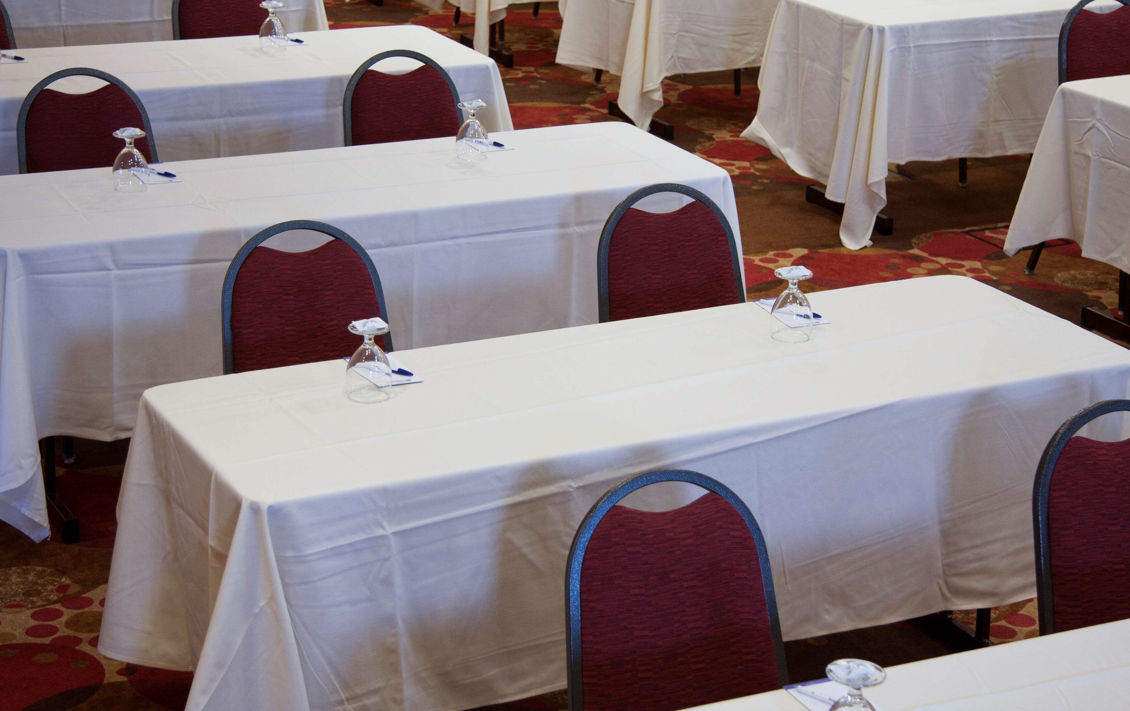 A conference room with multiple tables, each with a white tablecloth and a clear glass water bottle.