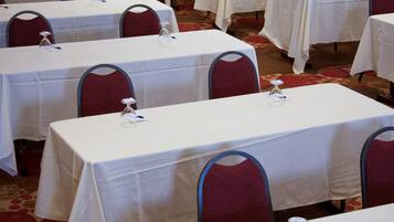 A conference room with multiple tables, each with a white tablecloth and a clear glass water bottle.