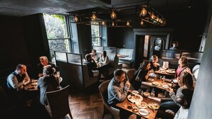 Un restaurant avec des tables et des chaises en bois, de grandes fenêtres et des luminaires suspendus.