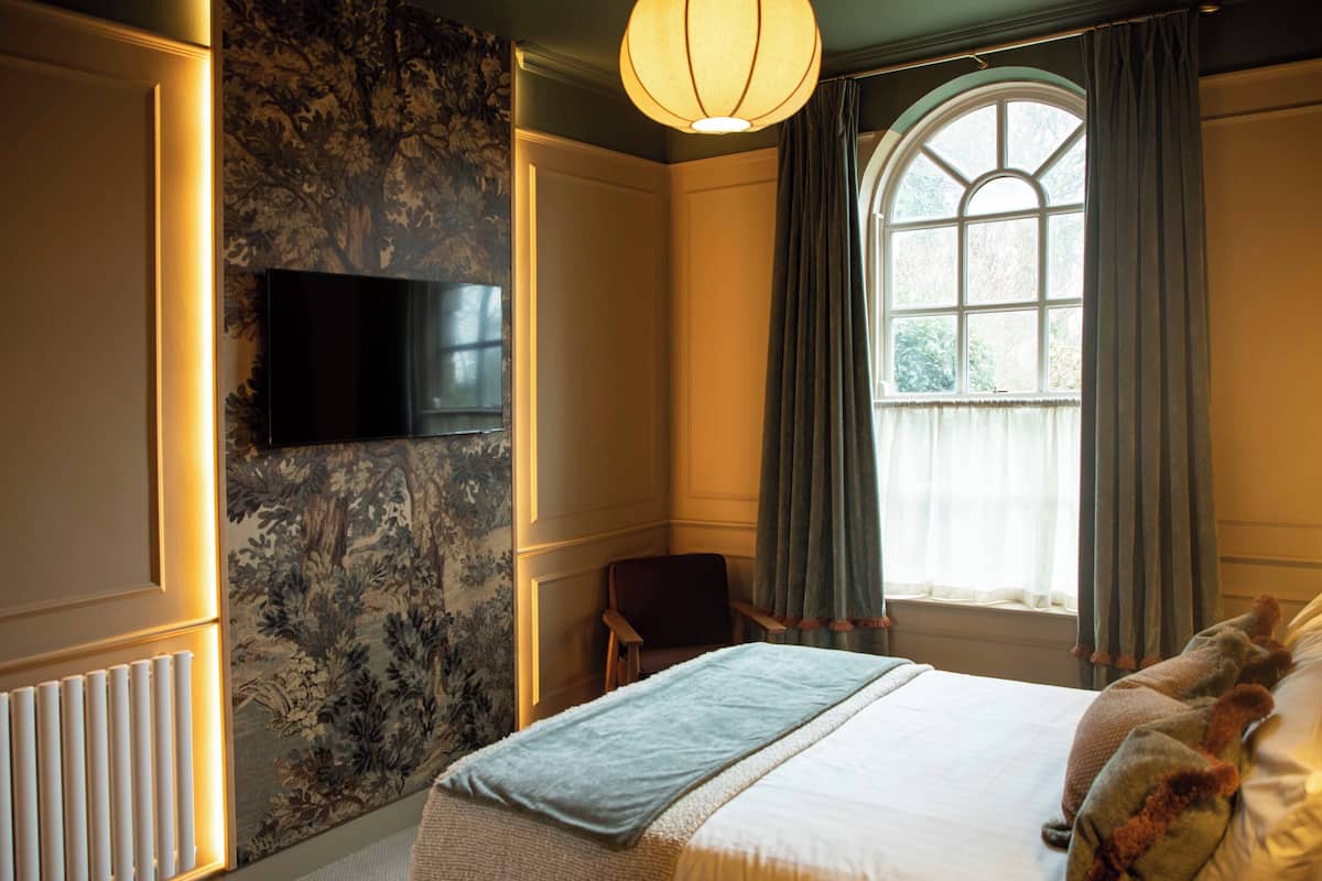 Habitación de hotel con una cama grande, un televisor de pantalla plana montado en la pared, una ventana con cortinas y un radiador.