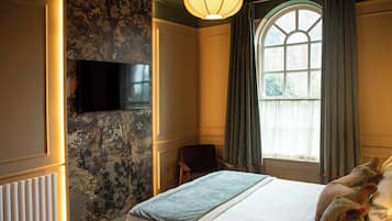 A hotel room with a large bed, a flat-screen TV mounted on the wall, a window with curtains, and a radiator.