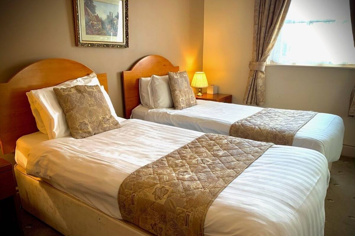 Habitación de hotel con dos camas, cada una con cabecera, lámpara de noche y un cuadro enmarcado en la pared.